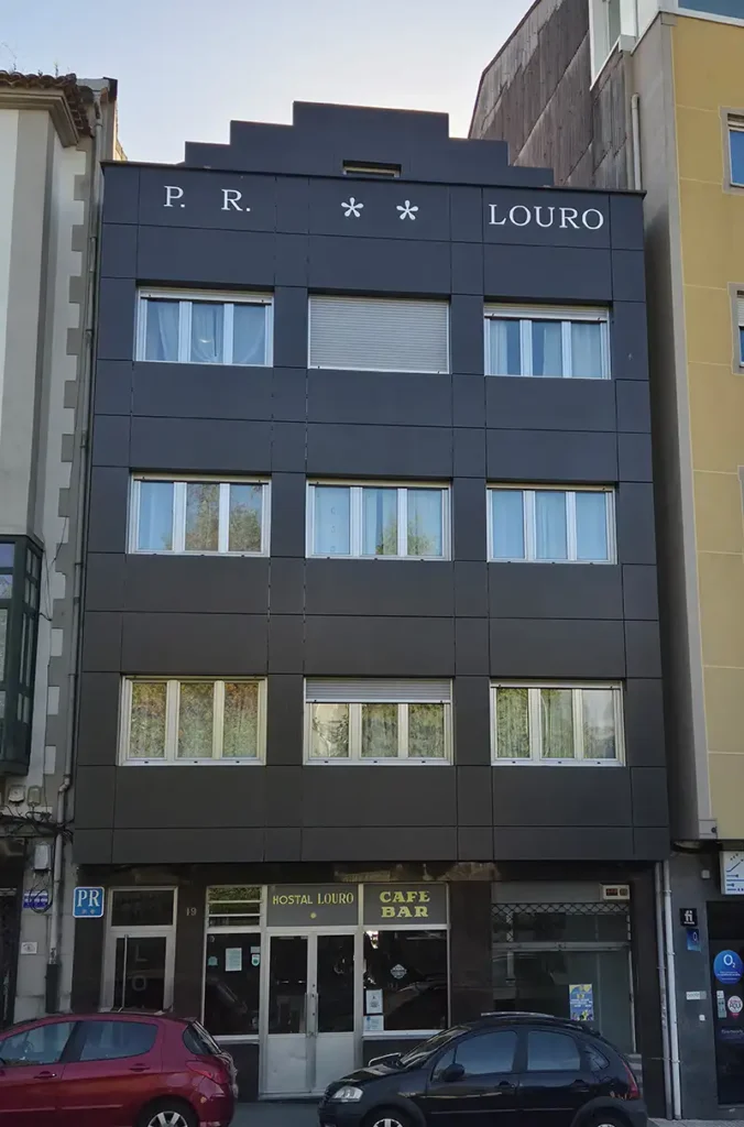 Fachada del Hostal Louro en Ordes, con el nombre del establecimiento en la parte superior y la entrada al alojamiento y café bar en la planta baja.
