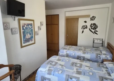 Habitación con dos camas independientes en el Hostal Louro en Ordes, con armario, mesilla y buena iluminación.